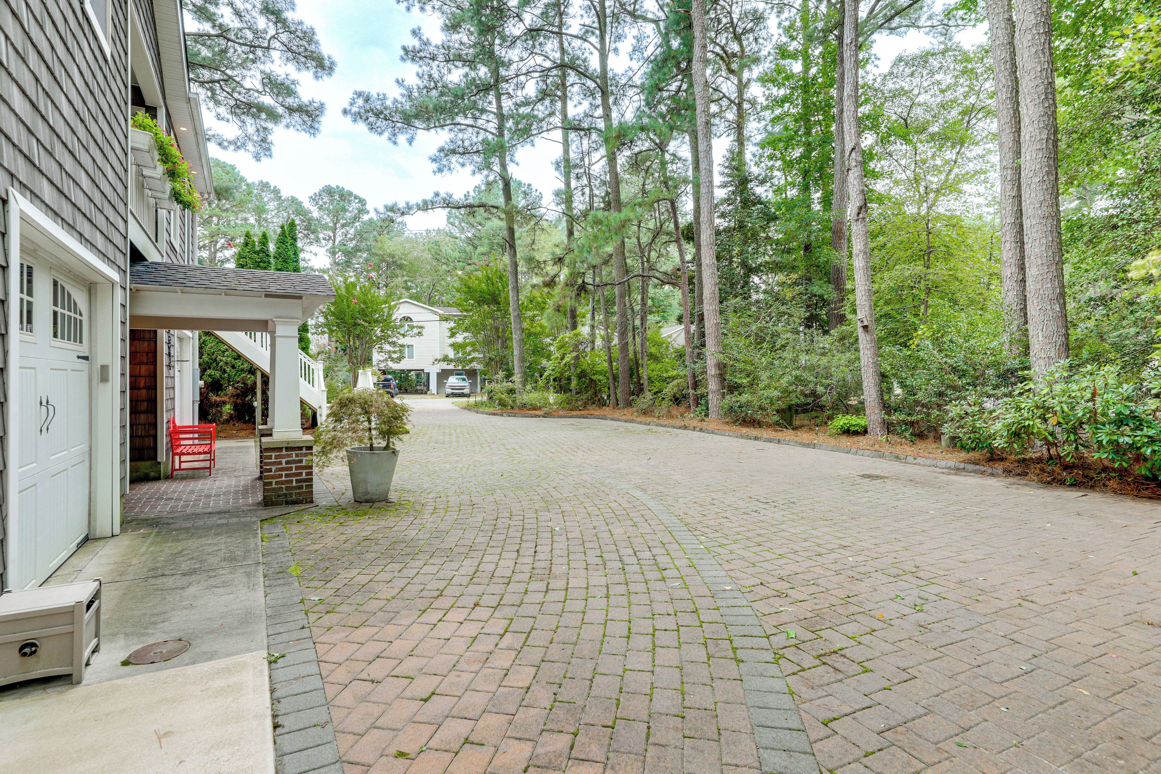 A paved driveway leading to a house with a covered porch, surrounded by tall trees and a well-maintained garden.