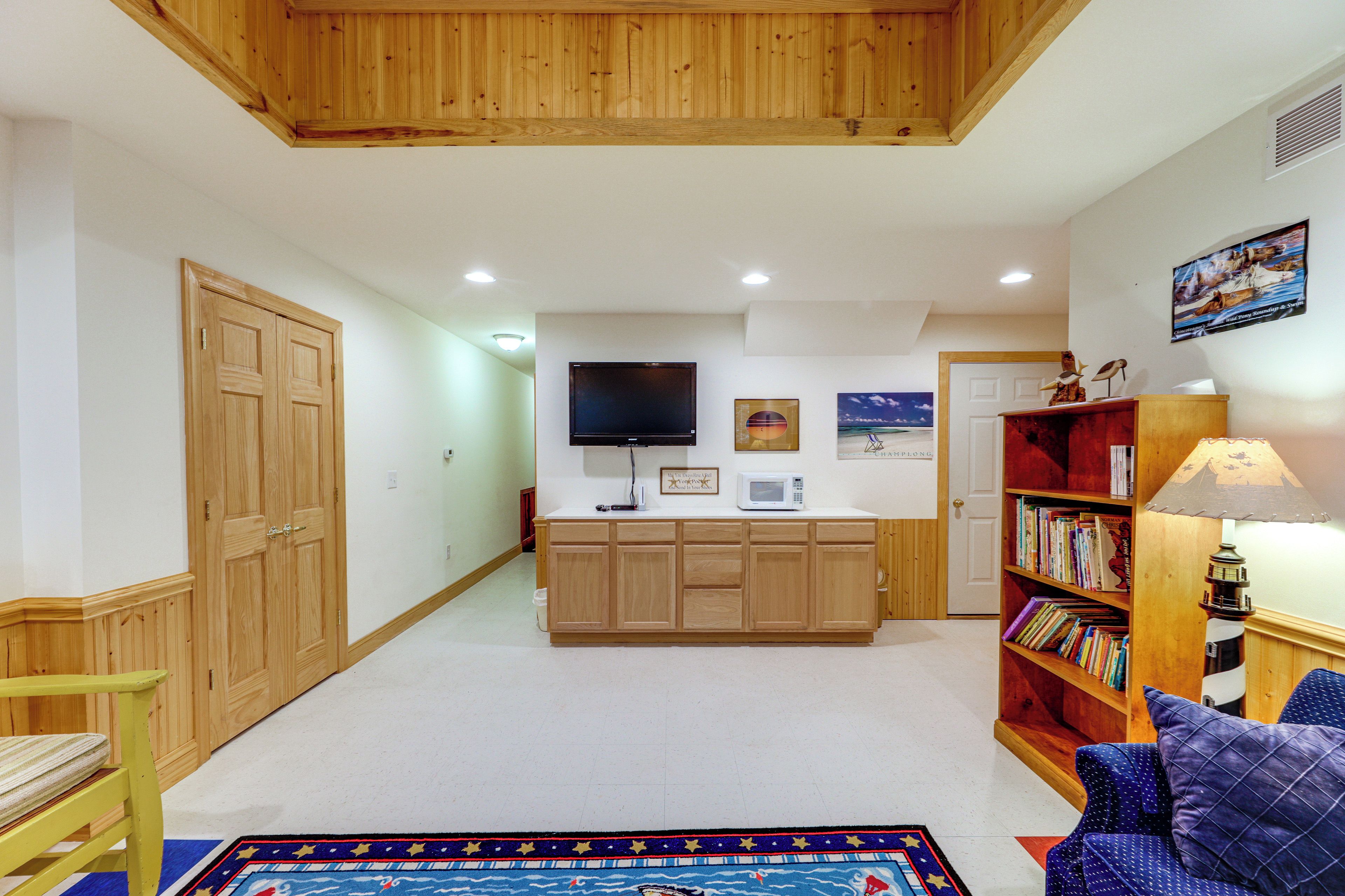 A spacious living area with a wooden ceiling, a television mounted on the wall, a bookshelf, and a patterned rug.