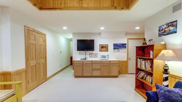 Un amplio salón con techo de madera, un televisor montado en la pared, una estantería y una alfombra estampada.