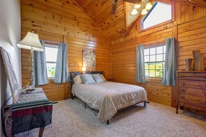 Ein gemütliches Schlafzimmer mit einem Bett, einer Kommode, einem Bild und einem Fenster mit Vorhängen.