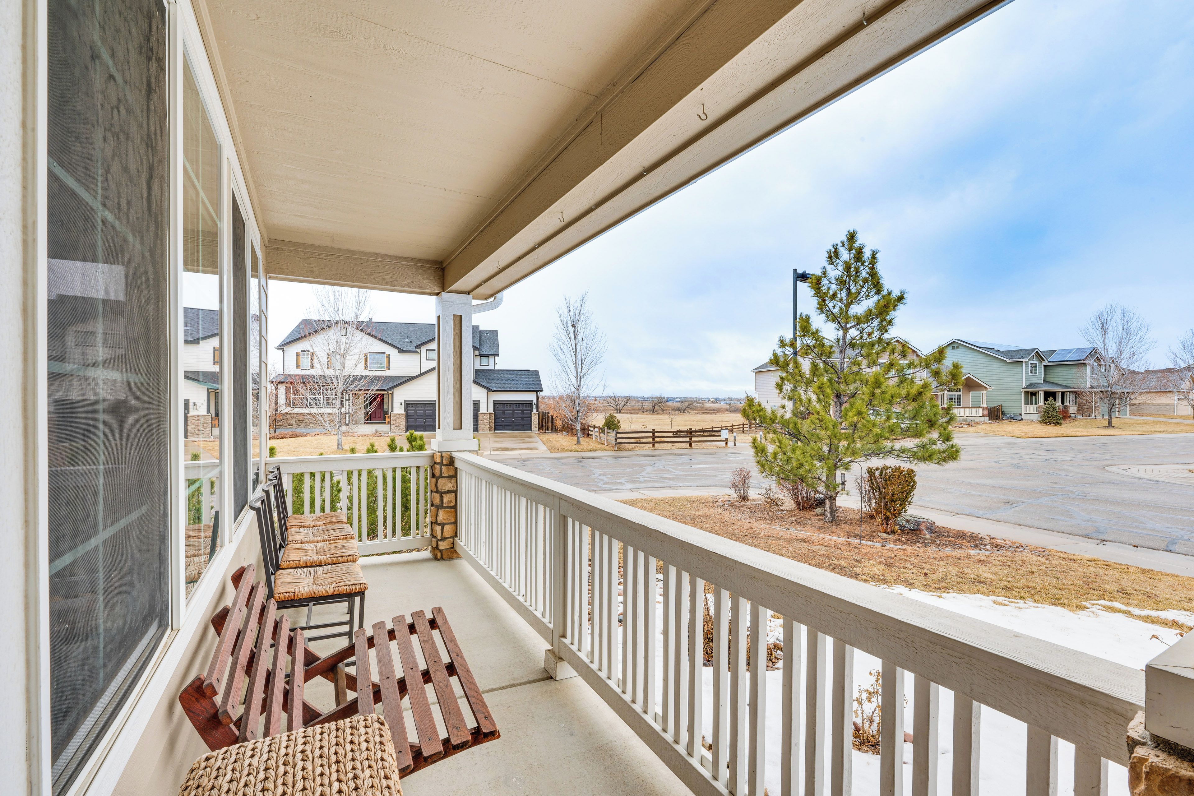 A covered porch with a bench and chairs, a view of a suburban neighborhood, and a clear sky.