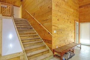 Una escalera de madera con barandilla, un banco y una puerta que da a otra habitación.