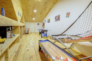 Una habitación con piso de madera, mesa de ping pong, sofá y zona de juegos con mosquitero.