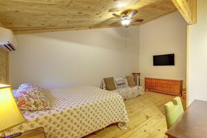 Un dormitorio con dos camas, un ventilador de techo, un televisor montado y un aparador de madera.