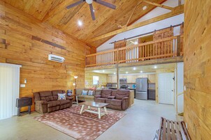 Un espacio habitable amplio con techo alto, paredes de madera, un balcón y una cocina al fondo.