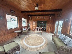 Interior de una cabaña de troncos con comedor, muebles de mimbre y un ventilador de techo.