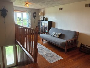 A living room with a wooden staircase, a sofa, a lamp, and a bookshelf. - 2BR + spacious loft. Rich Hill Retreat offers spectacular mountain view. (Connellsville)