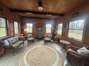 A cozy room with a wooden ceiling, large windows, and a stone fireplace. There are wicker furniture pieces and a woven rug. - 2BR + spacious loft. Rich Hill Retreat offers spectacular mountain view. (Connellsville)