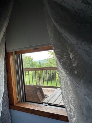 Una habitación con ventana que da a una terraza de madera y un paisaje verde.