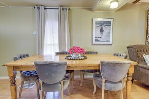 A dining area with a wooden table, grey upholstered chairs, a vase with pink flowers, and a framed picture on the wall.