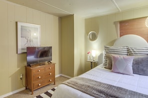 Une chambre à coucher comprenant un lit, une commode, un téléviseur, un miroir et une petite table avec une lampe.