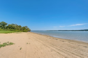 Uma praia arenosa com águas calmas, árvores e céu limpo.