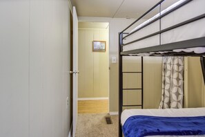 Uma cama beliche com cobertor azul, uma porta que dá para um quarto com piso de madeira e uma cortina com desenho circular.