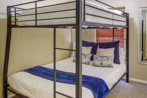 Un lit superposé avec une structure en métal, une literie blanche et des coussins décoratifs.