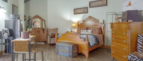 A bedroom with a wooden bed, dresser, and a chair. There is a small table with a lamp and a decorative mirror.