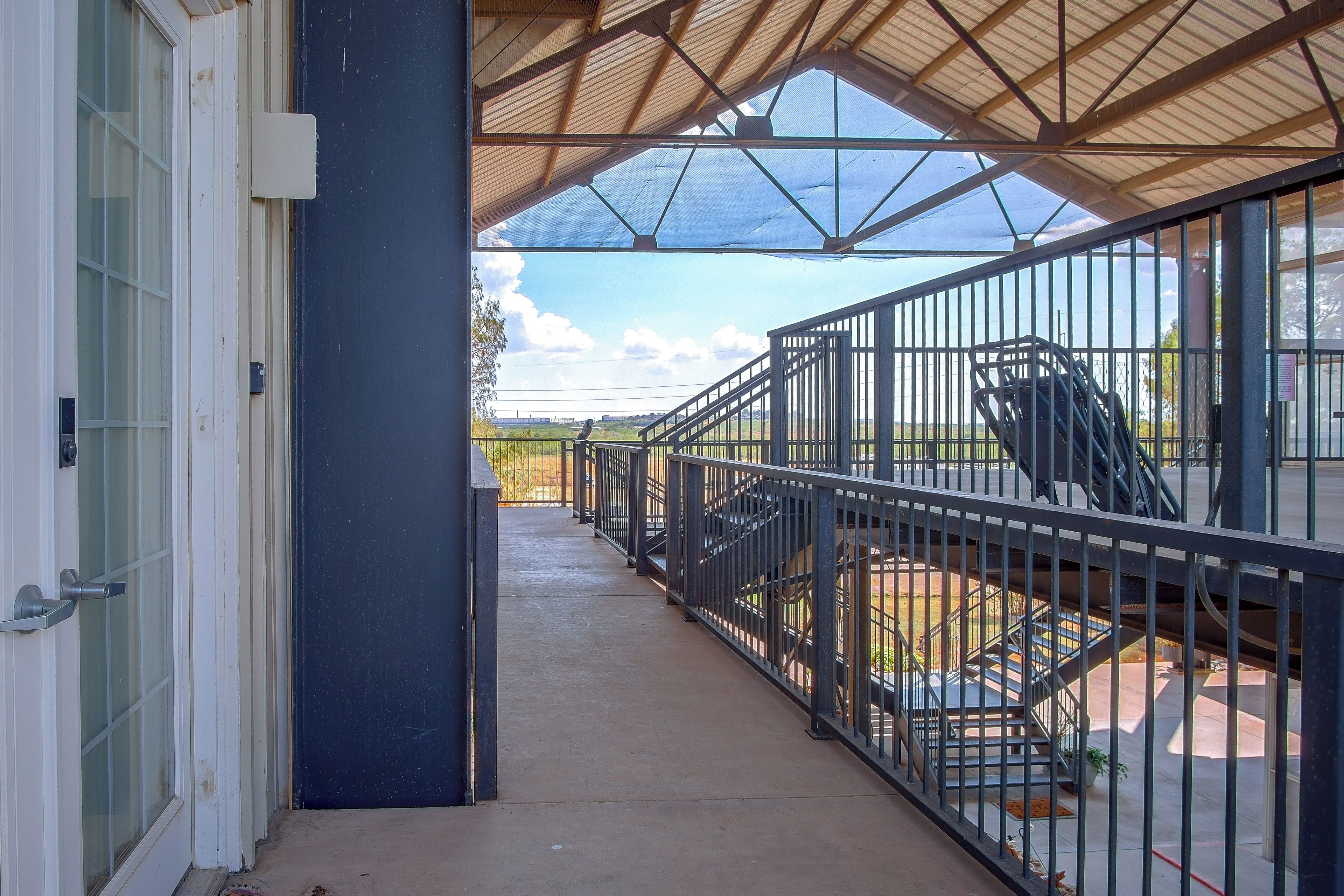 A covered outdoor area with a metal railing, a concrete floor, and a view of the landscape.