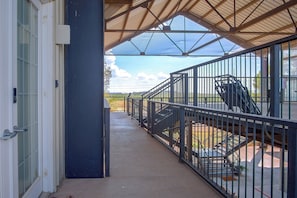 Un espacio al aire libre techado con barandilla metálica, suelo de concreto y vista del paisaje.
