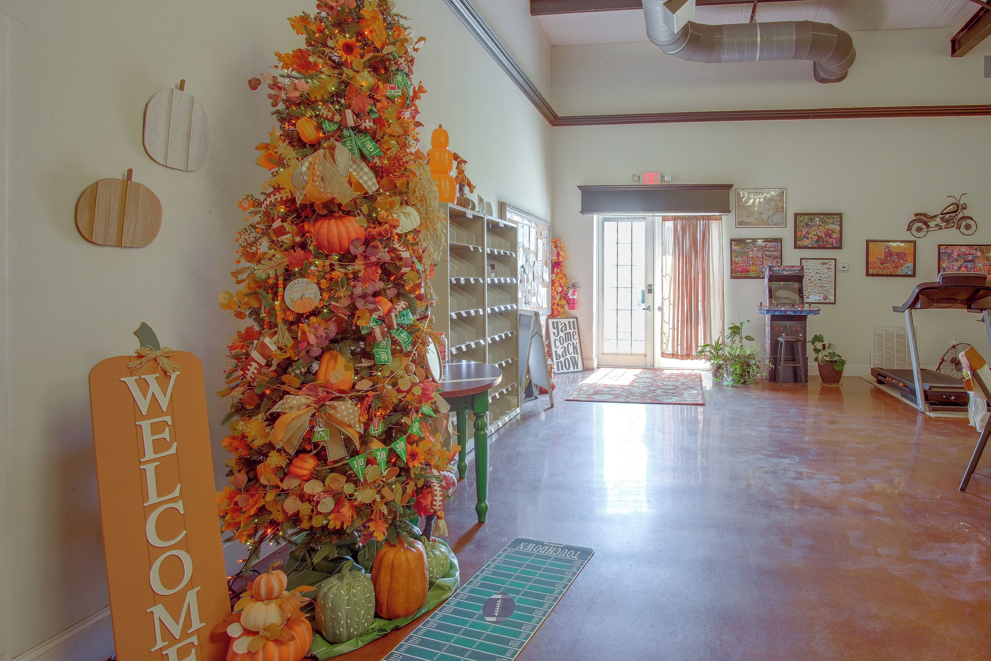 Un área de recepción con un muro decorado con motivos otoñales, un letrero de bienvenida, un tablón de anuncios y una caminadora.