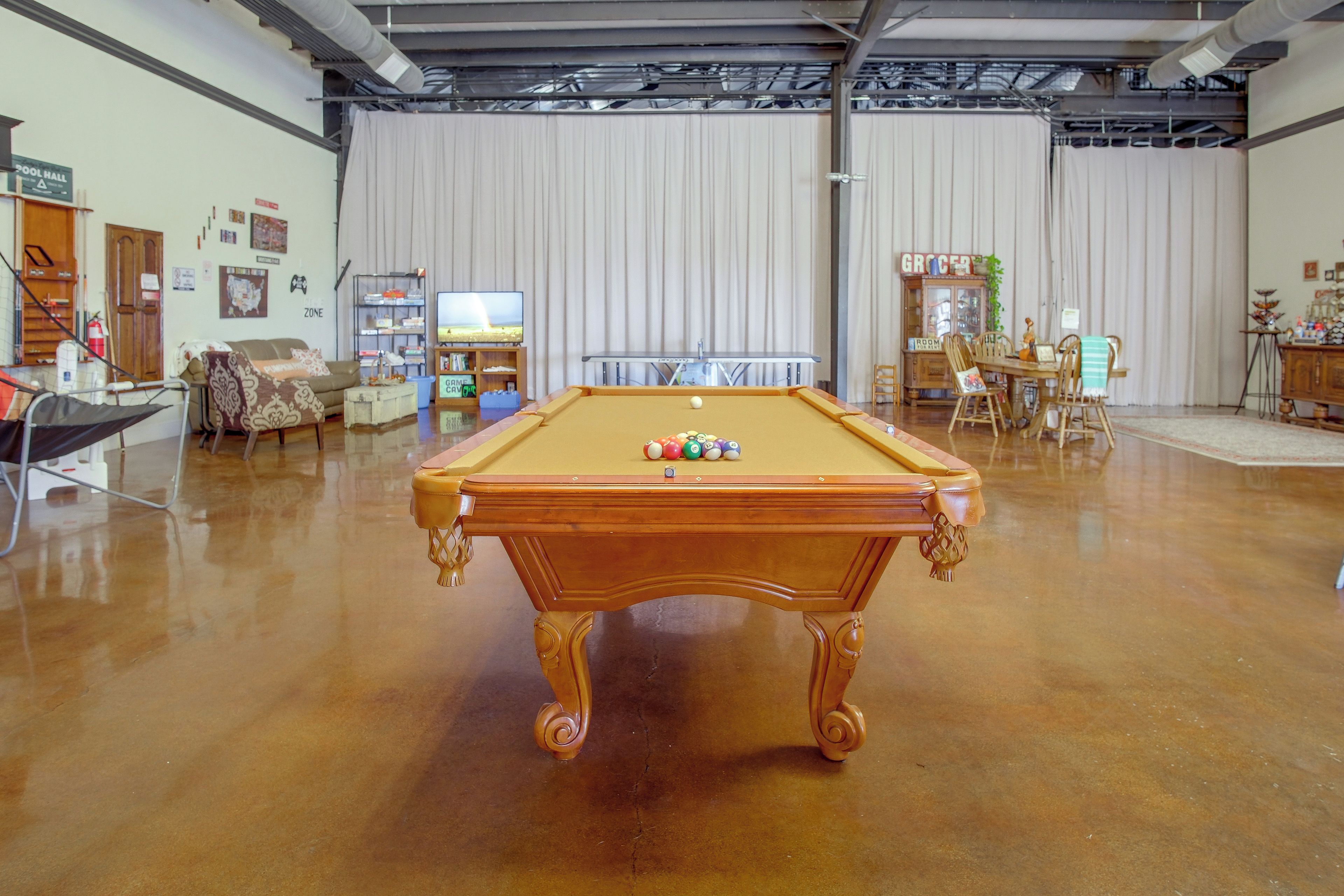A billiards table in a room with a pool table, a television, and various items on shelves.