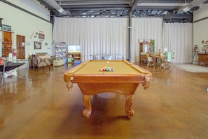 Una mesa de billar en una sala con mesa de snooker, televisor y varios objetos en estanterías.