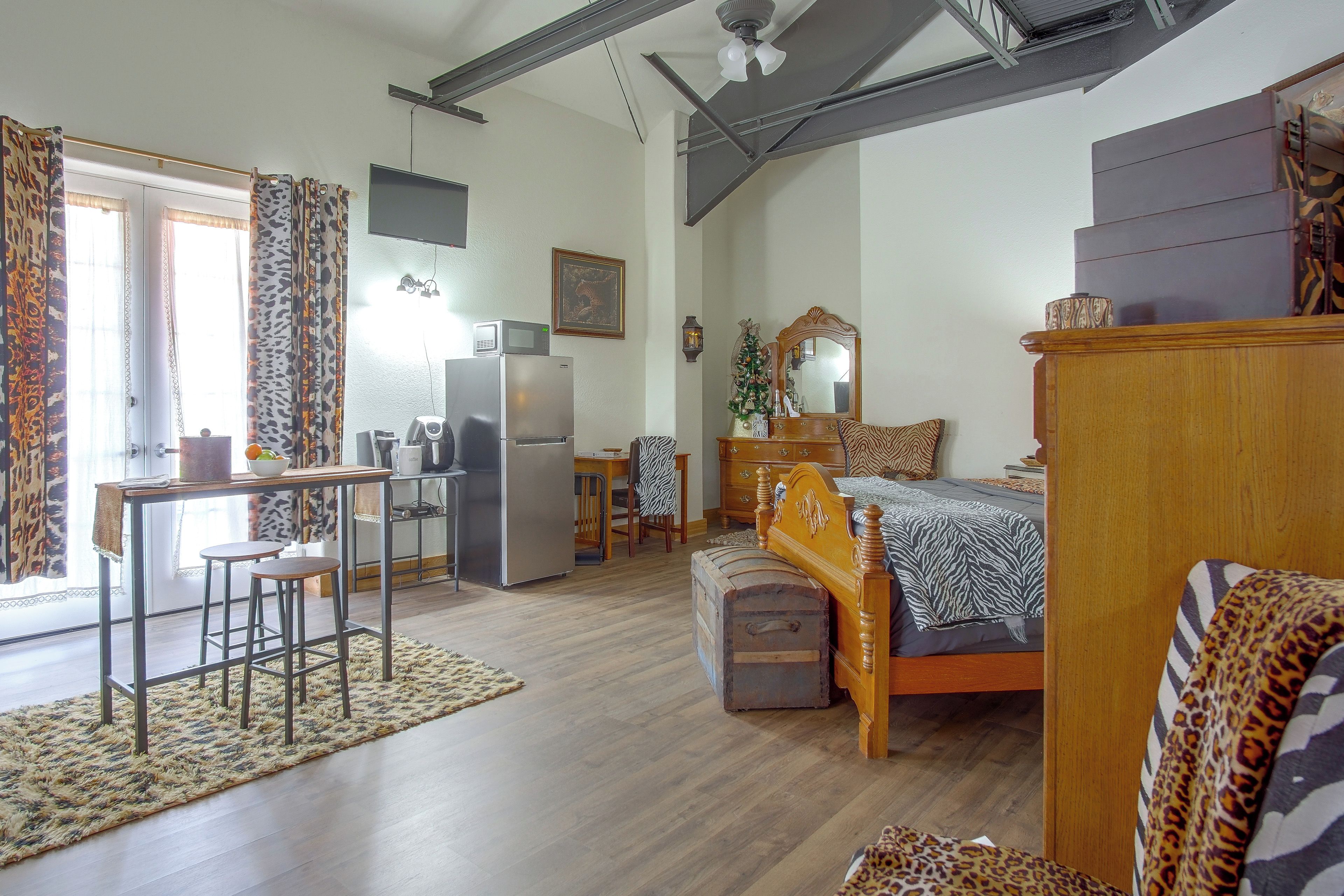 Un espacio habitable compacto con kitchenette, una cama con colcha de estampado de cebra, un aparador de madera y un área de comedor con mesa y sillas.