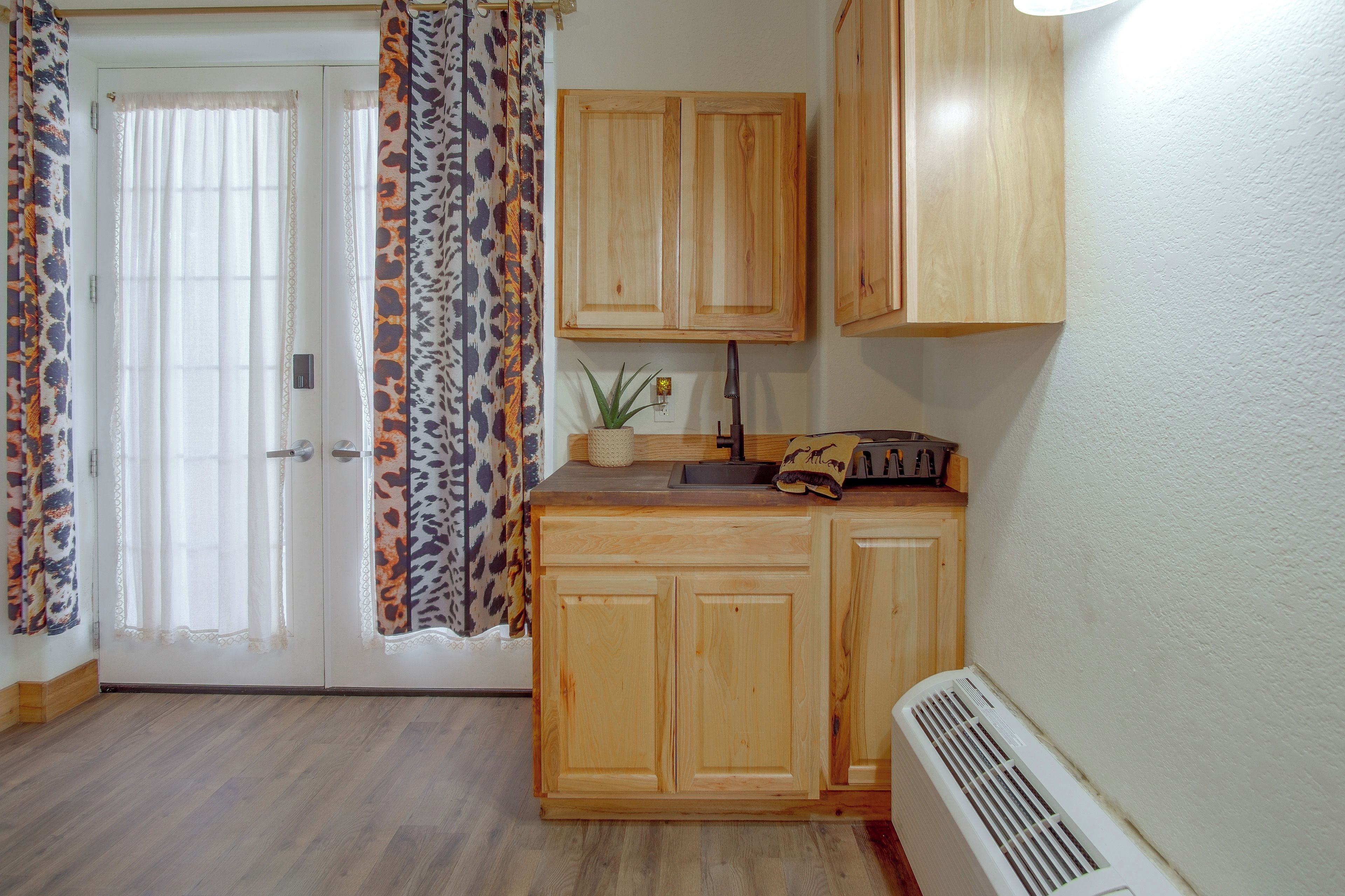 A kitchen with wooden cabinets, a sink, a countertop, and a window with patterned curtains.