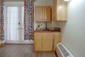 A kitchen with wooden cabinets, a sink, a countertop, and a window with patterned curtains. - Denton Couples' Studio on 100-acre Ranch (Denton)