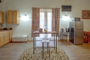 A compact kitchen with wooden cabinets, a built-in microwave, a refrigerator, and a dining area with a table and two stools.