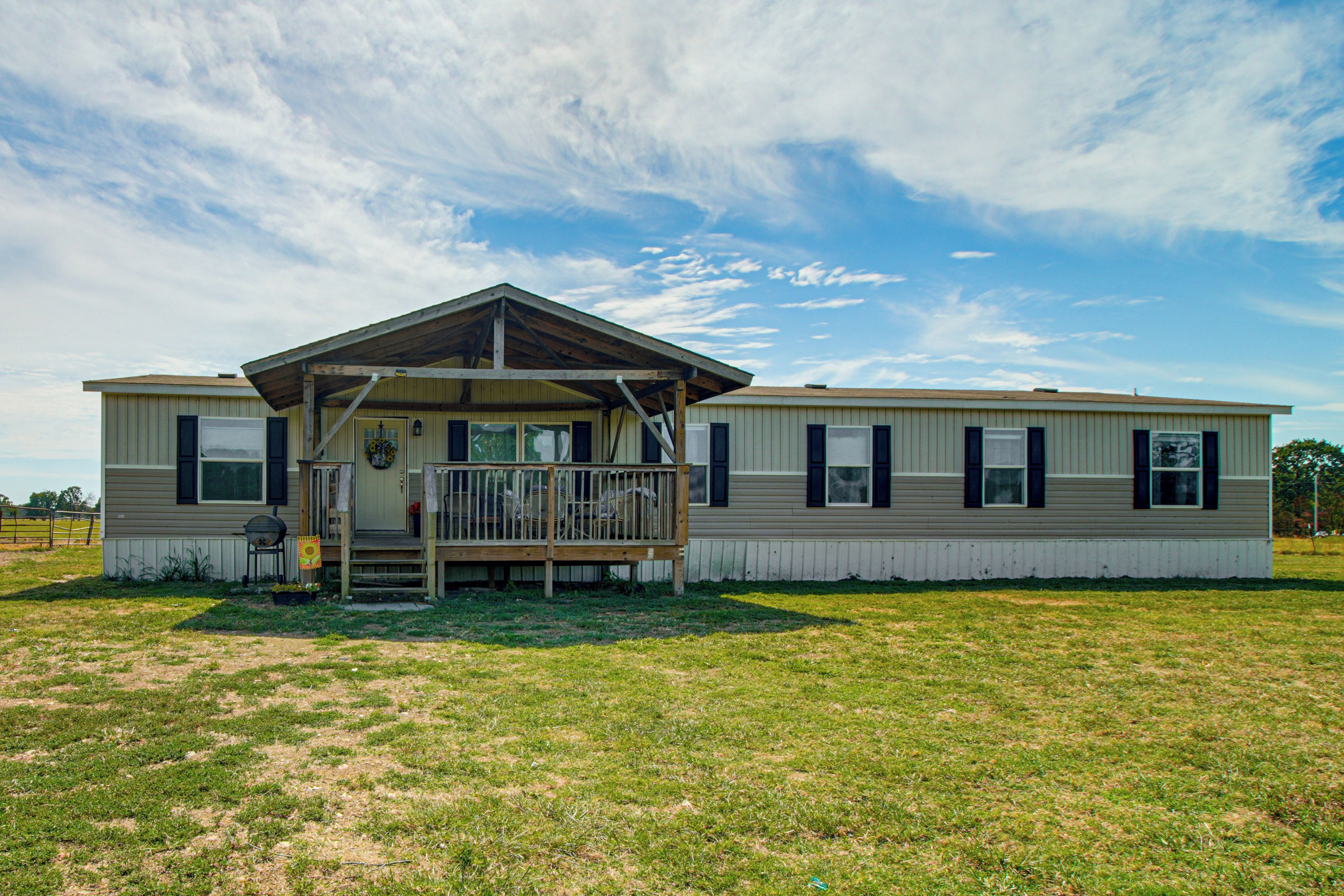 A two-story mobile home with a covered porch and a fenced yard.