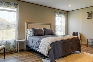 Un dormitorio con cama, mesita de noche, una silla y ventana con cortinas.