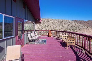 Una terraza de madera con mobiliario exterior, un ventanal grande y vistas a un paisaje desértico.