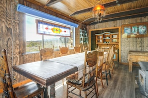 A rustic dining room with a large wooden table and chairs, a stained glass window, and wooden shelves with decorative items. - ATV Adventures & Private Pond! Marysvale Retreat (Marysvale)