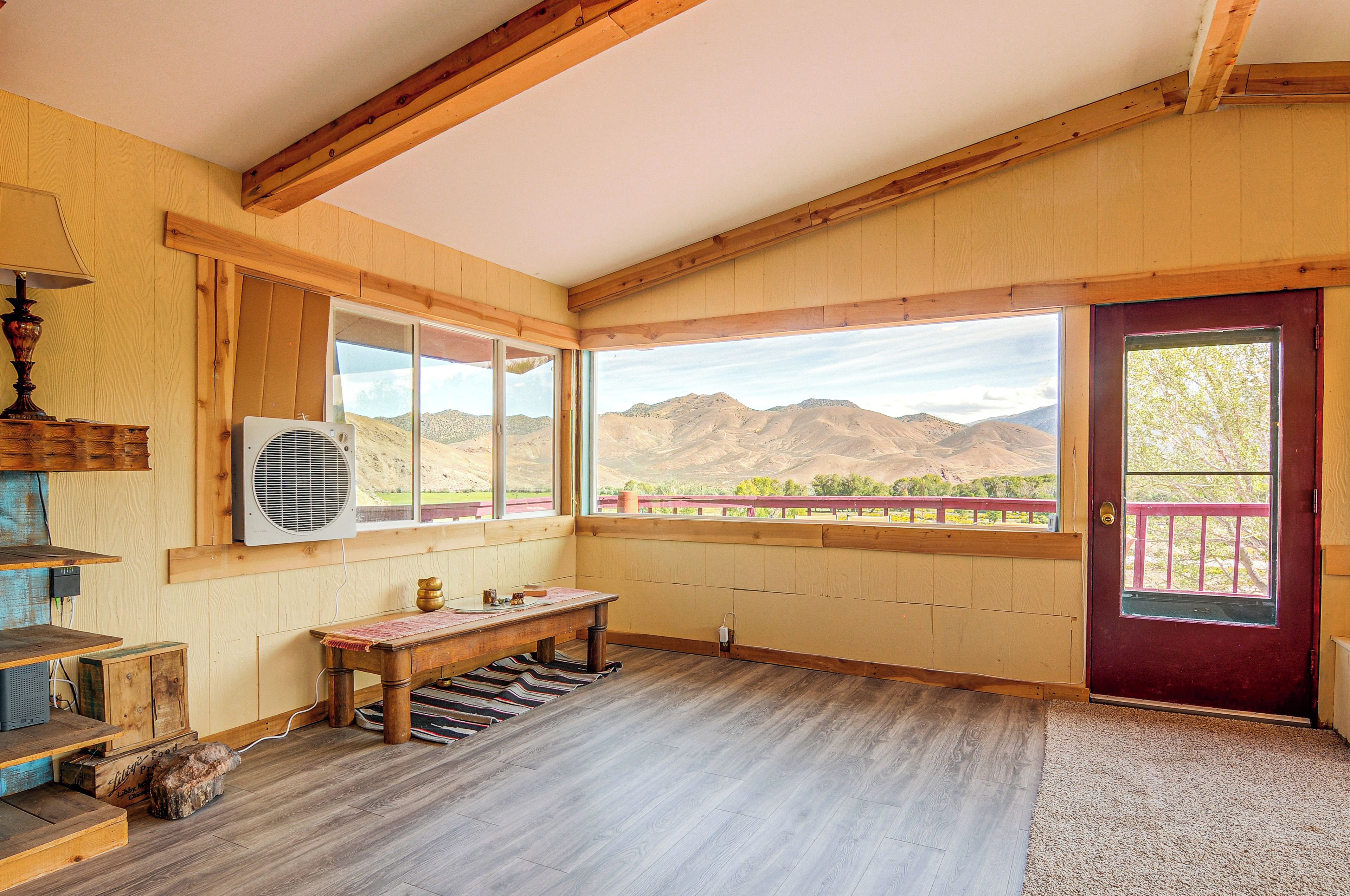 A room with wooden beams, a large window with a view of mountains, a red door, and a bench.