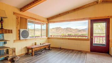 A room with wooden beams, a large window with a view of mountains, a red door, and a bench.