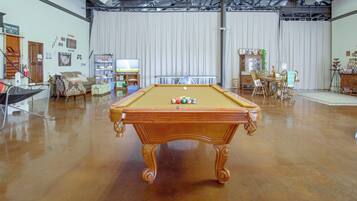 A spacious room with a pool table, a television, and a gaming area.