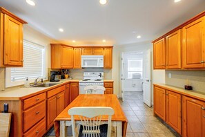 A kitchen with wooden cabinets, a white stove, and a dining table with chairs. - Naples Duplex Bundle By Shopping & Beaches (Naples)