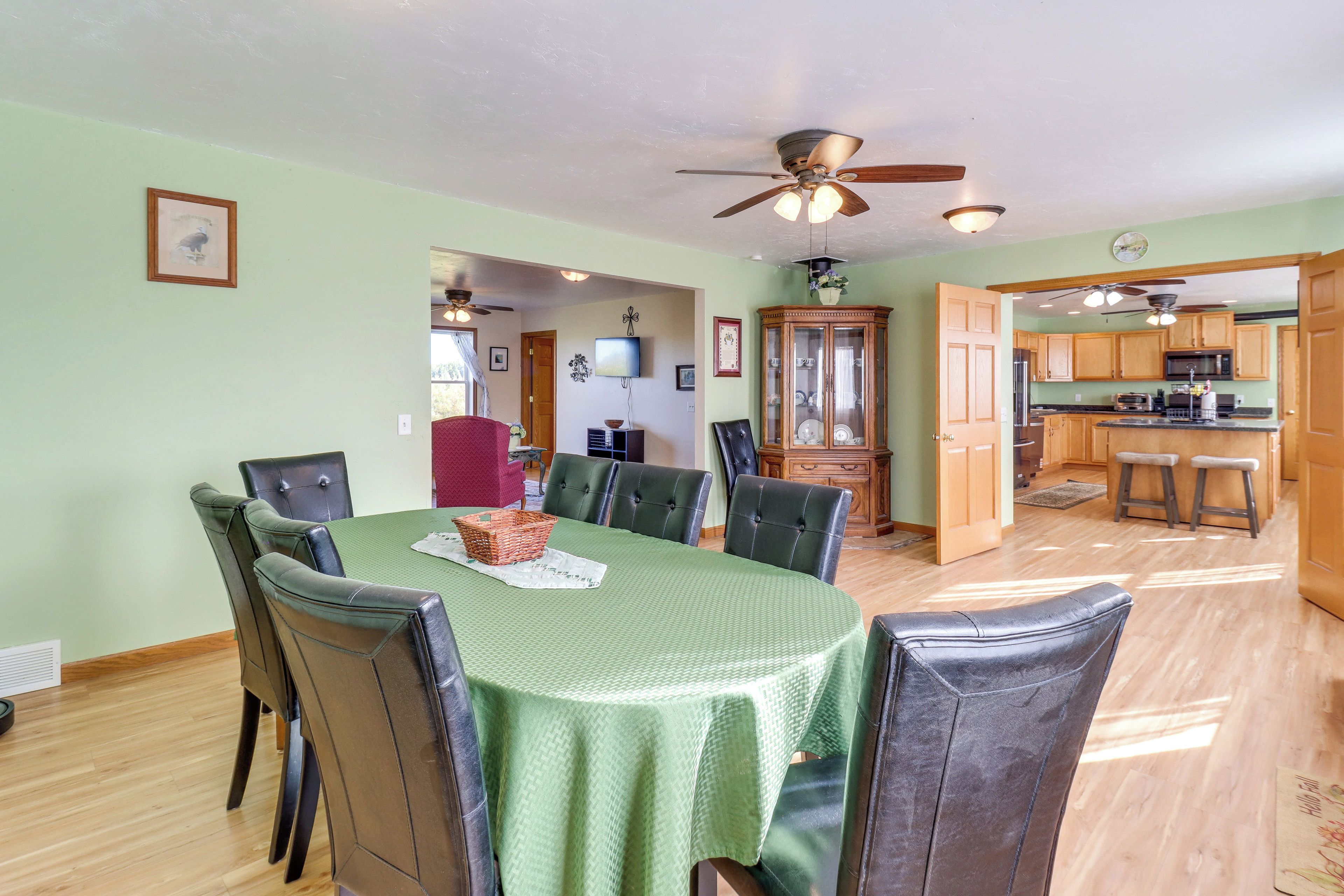 A dining area with a green tablecloth, leather chairs, and a ceiling fan.