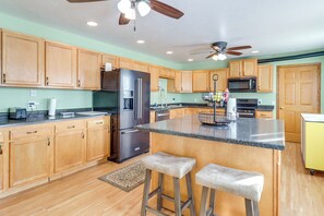 A modern kitchen with wooden cabinets, a stainless steel refrigerator, a microwave, and a ceiling fan.