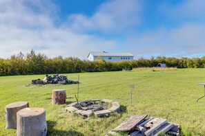 A grassy field with a house, a fire pit, and a picnic table.