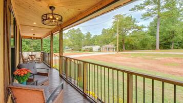A covered porch with outdoor seating, a view of a baseball field, and surrounding trees.
