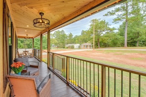 A covered porch with outdoor seating, a view of a baseball field, and surrounding trees.