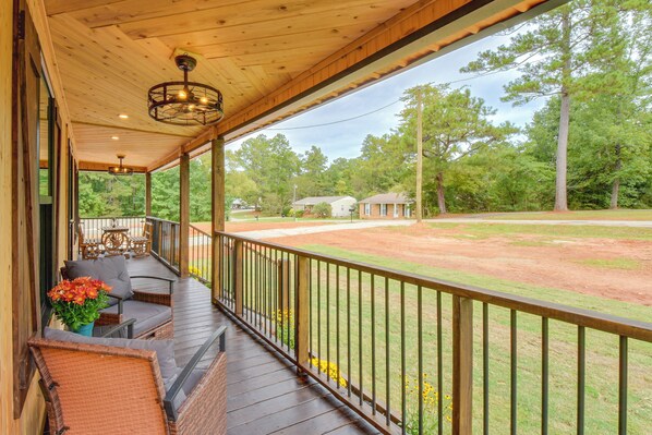 A covered porch with outdoor seating, a view of a baseball field, and surrounding trees.