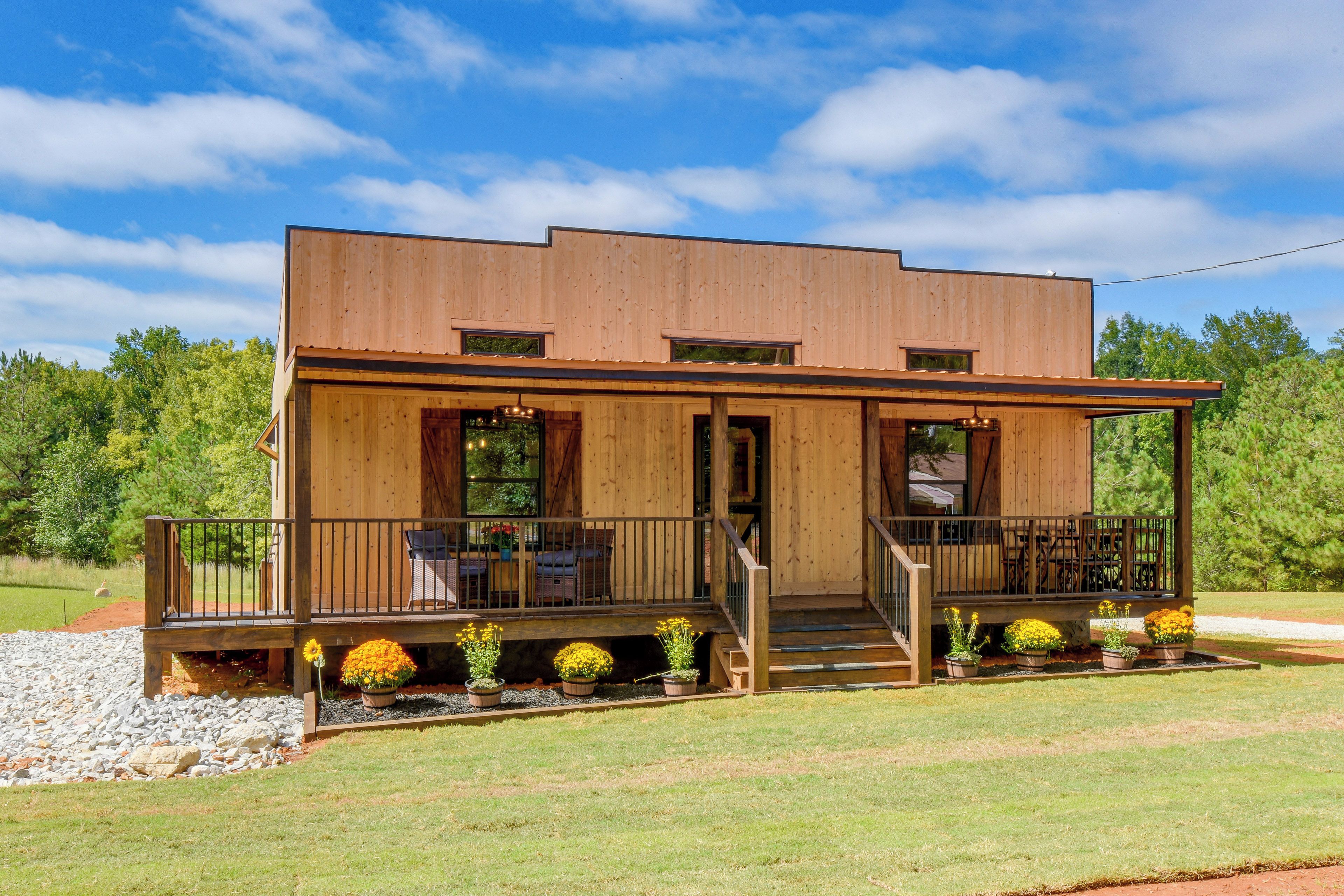 A two-story wooden cabin with a porch, outdoor seating, and a small garden.