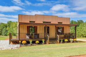 A two-story wooden cabin with a porch, outdoor seating, and a small garden.