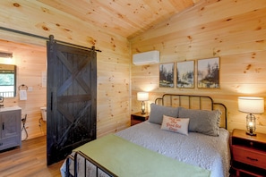 A wooden cabin bedroom with a bed, two bedside tables with lamps, a sliding door, and a mounted air conditioner.