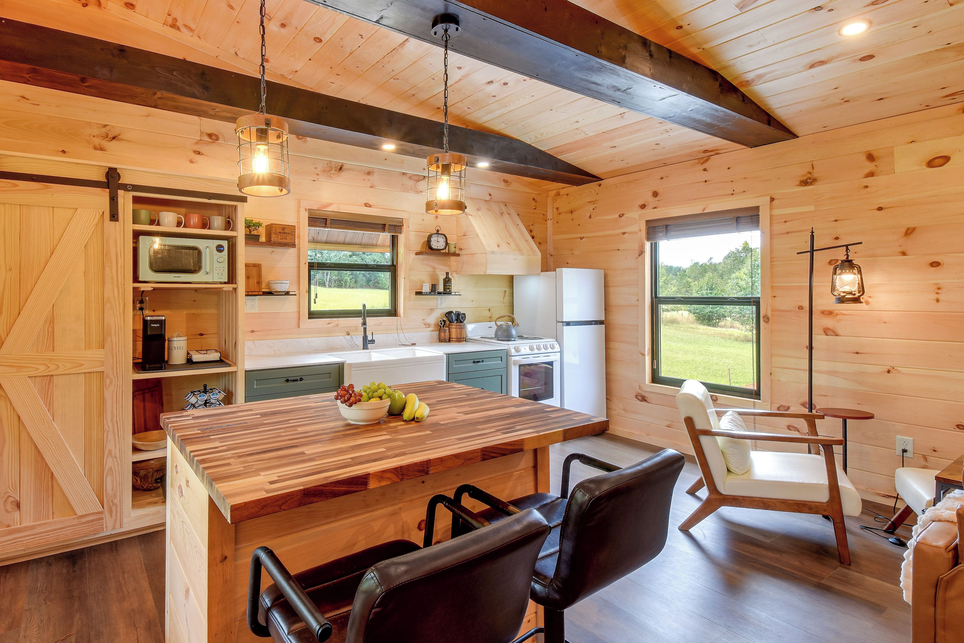 A wooden interior with a kitchen area featuring a wooden table, chairs, a microwave, and a refrigerator.