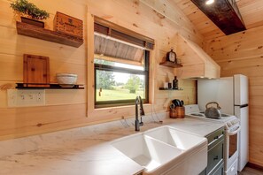 A kitchen with wooden walls, a marble countertop, a sink, a stove, and a window with a view of greenery.