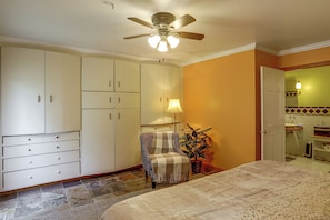 A bedroom with a bed, a chair, a ceiling fan, a lamp, and a bathroom visible through an open door. - Nature Lover's Cottage on Wooded Acreage (Nova)