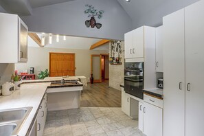 A modern kitchen with white cabinetry, a central island, and a dining area with a red door. - Nature Lover's Cottage on Wooded Acreage (Nova)