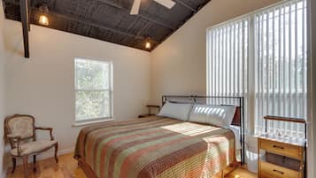 A bedroom with a bed, a chair, a bedside table, a window with blinds, and a ceiling fan.